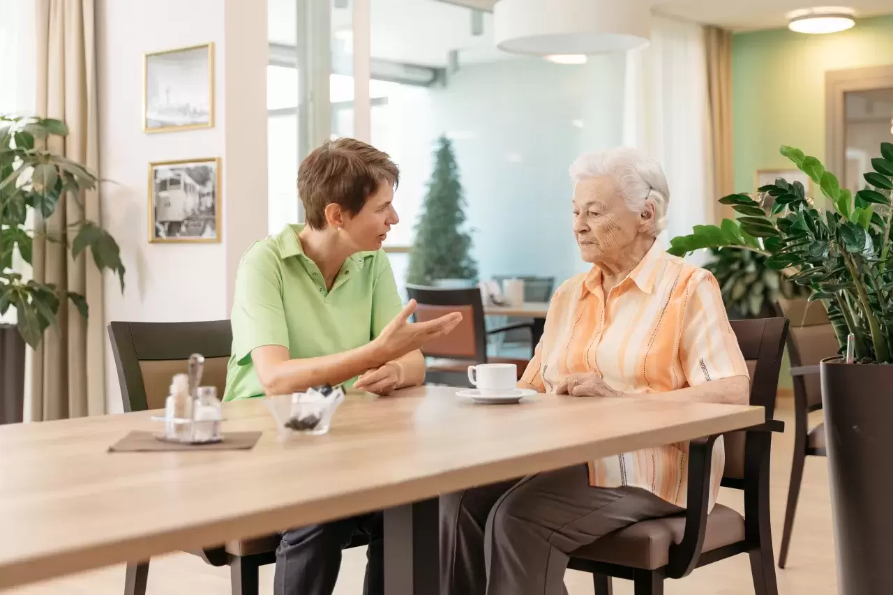 Eine Seniorin und eine Pflegehelfende sitzen gemeinsam am Tisch.