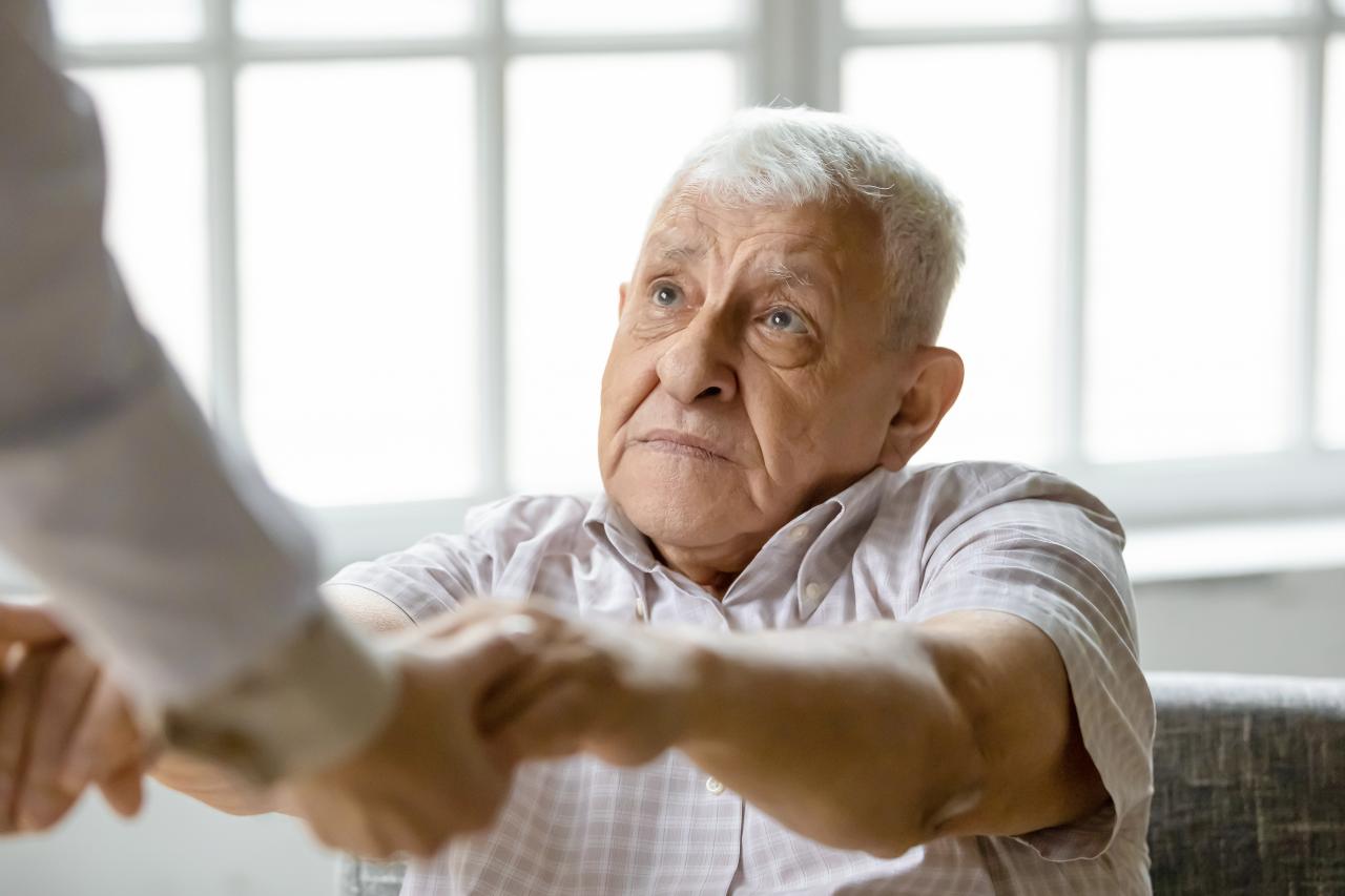Betreuerin reicht einem traurigen Senior die Hände