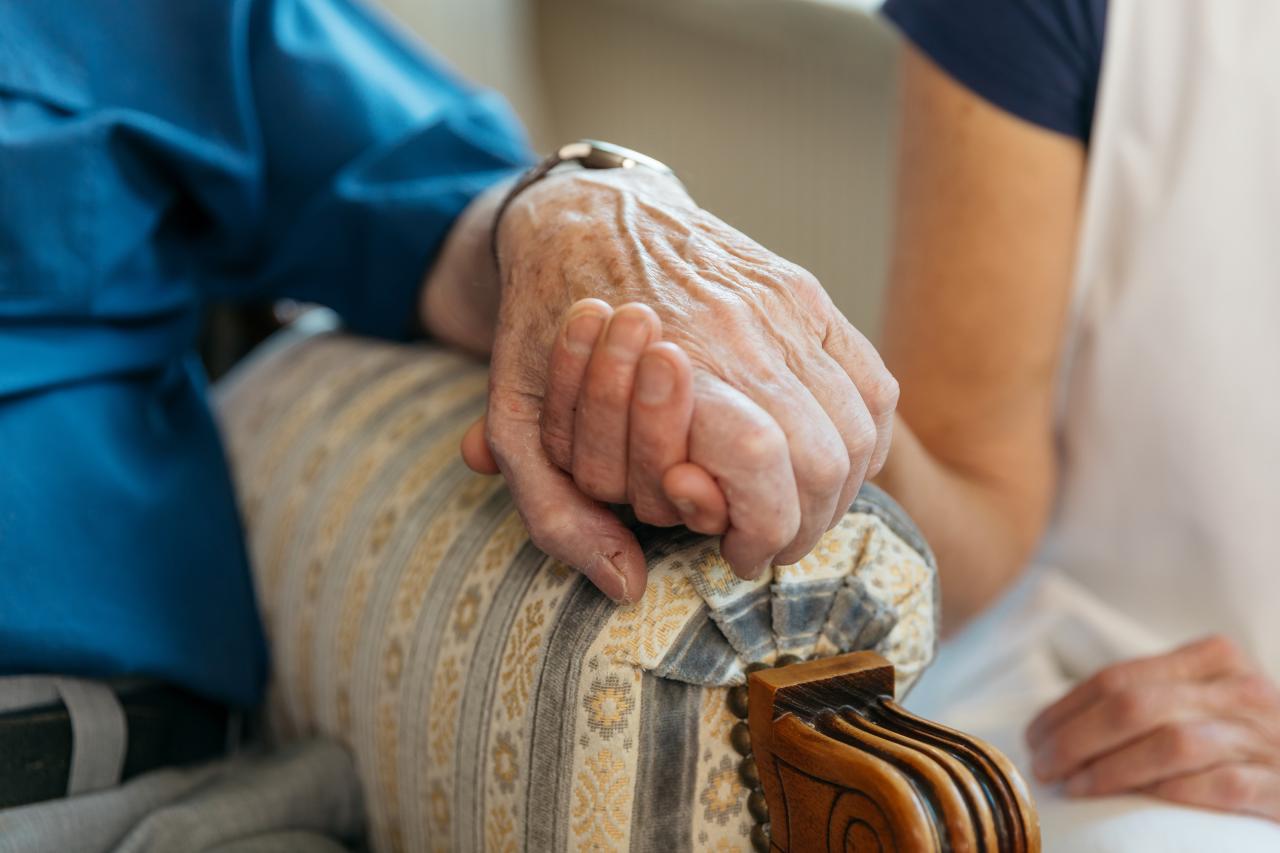 Close-up von einer jüngeren Person, die einer betagten Person die Hand hält.