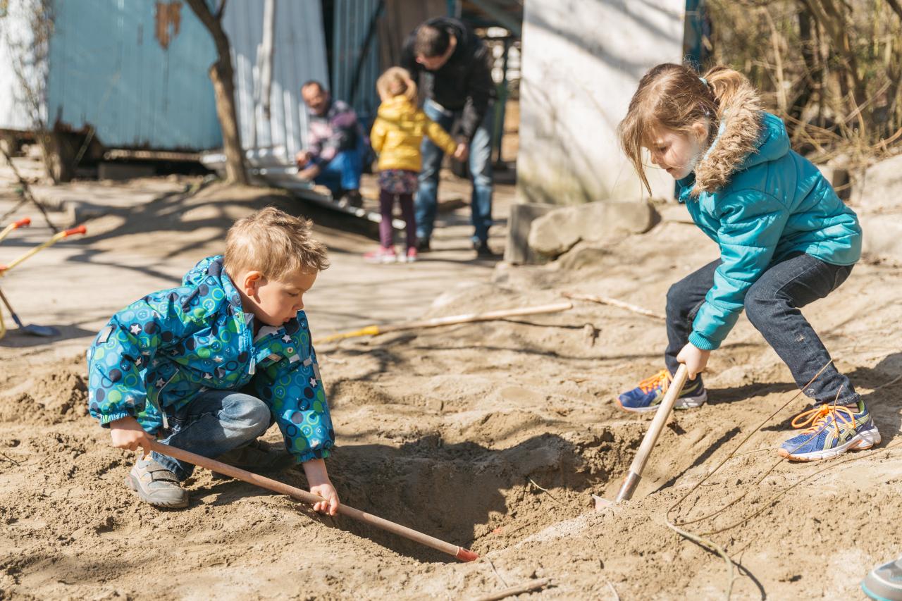 Zwei Kinder spielen zusammen im Sandkasten und graben ein Loch