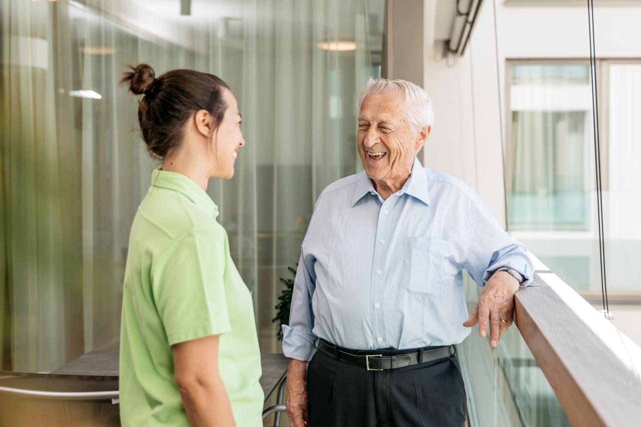 Eine junge Pflegehelfende im Gespräch mit einem Patienten