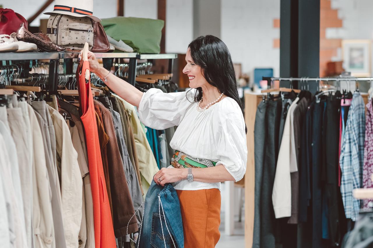 Eine Frau kauft in einem Secondhand-Shop ein und schaut sich ein Kleid an