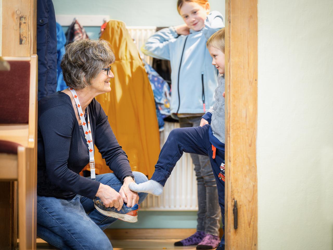 Eine Kinderbetreuerin des SRK Kanton Bern hilft einem Kind beim Anziehen der Schuhe.