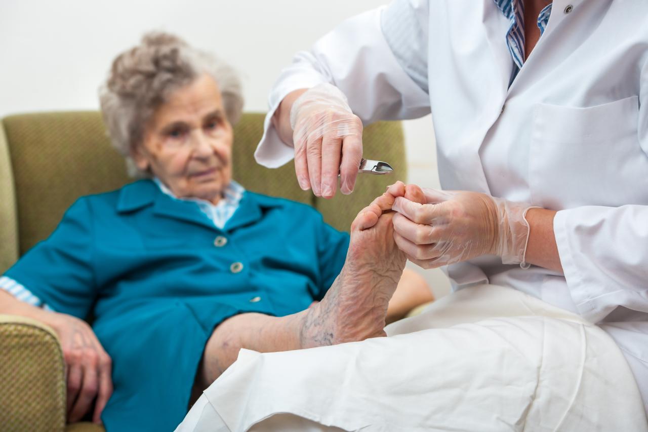 Eine Pflegehelfende pflegt die Füsse einer älteren Dame.