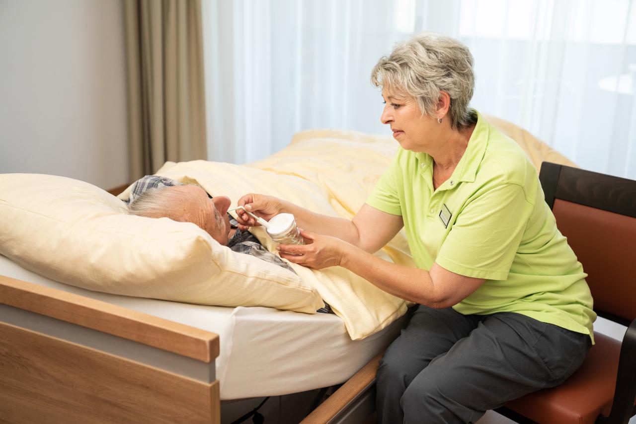 Pflegehelferin reicht dem Patienten Wasser