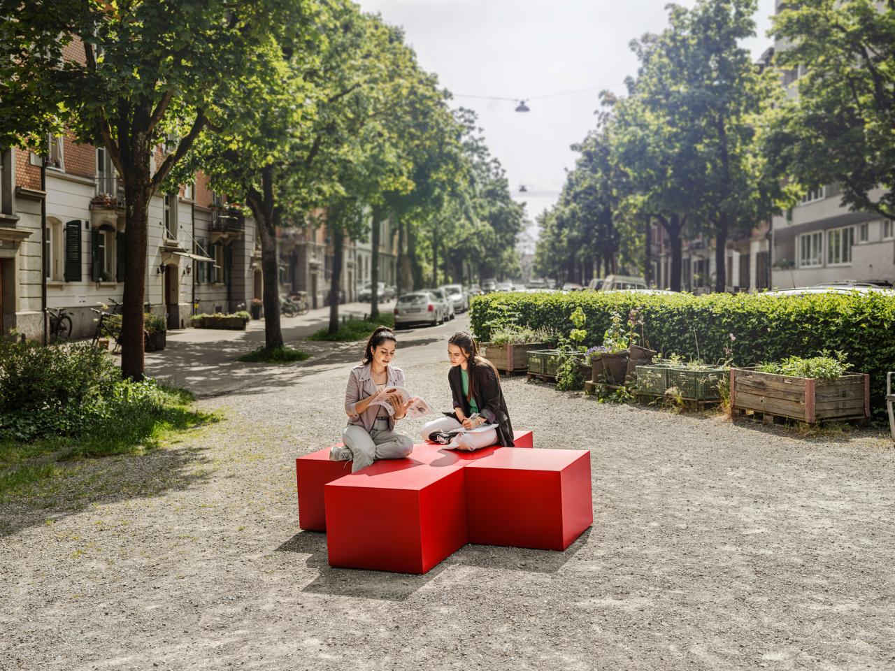 Zwei junge Frauen sitzen in der Stadt auf einem roten Kreuz und lernen zusammen.