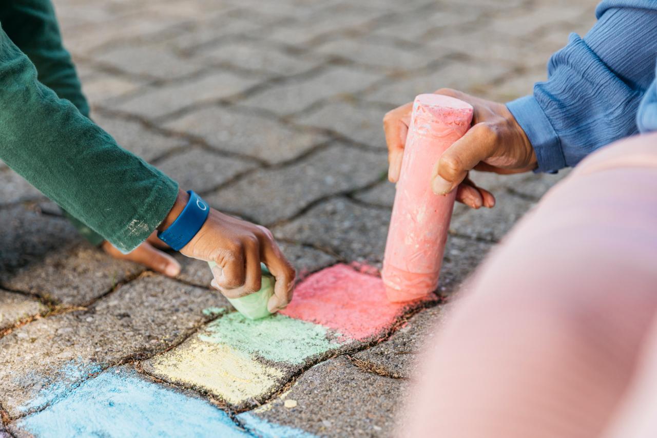 Eine Kinder- und eine Frauenhand malen mit Strasesnkreide