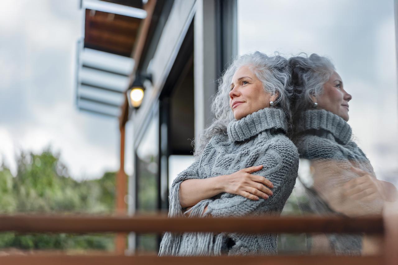 Eine Frau lehnt sich an Balkontür und blickt in die Ferne