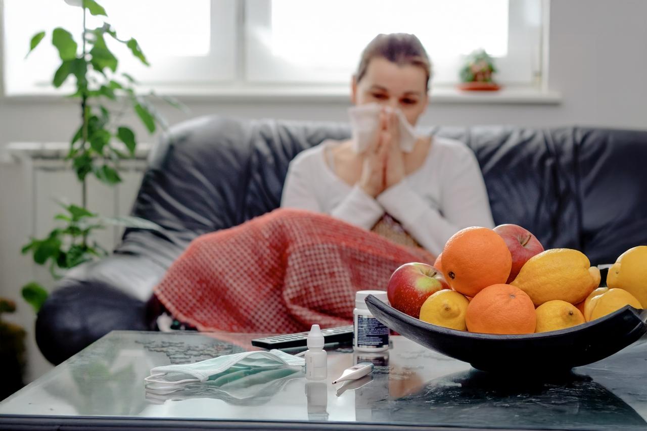 Eine Frau sitzt erkältet auf dem Sofa und schnäuzt sich die Nase