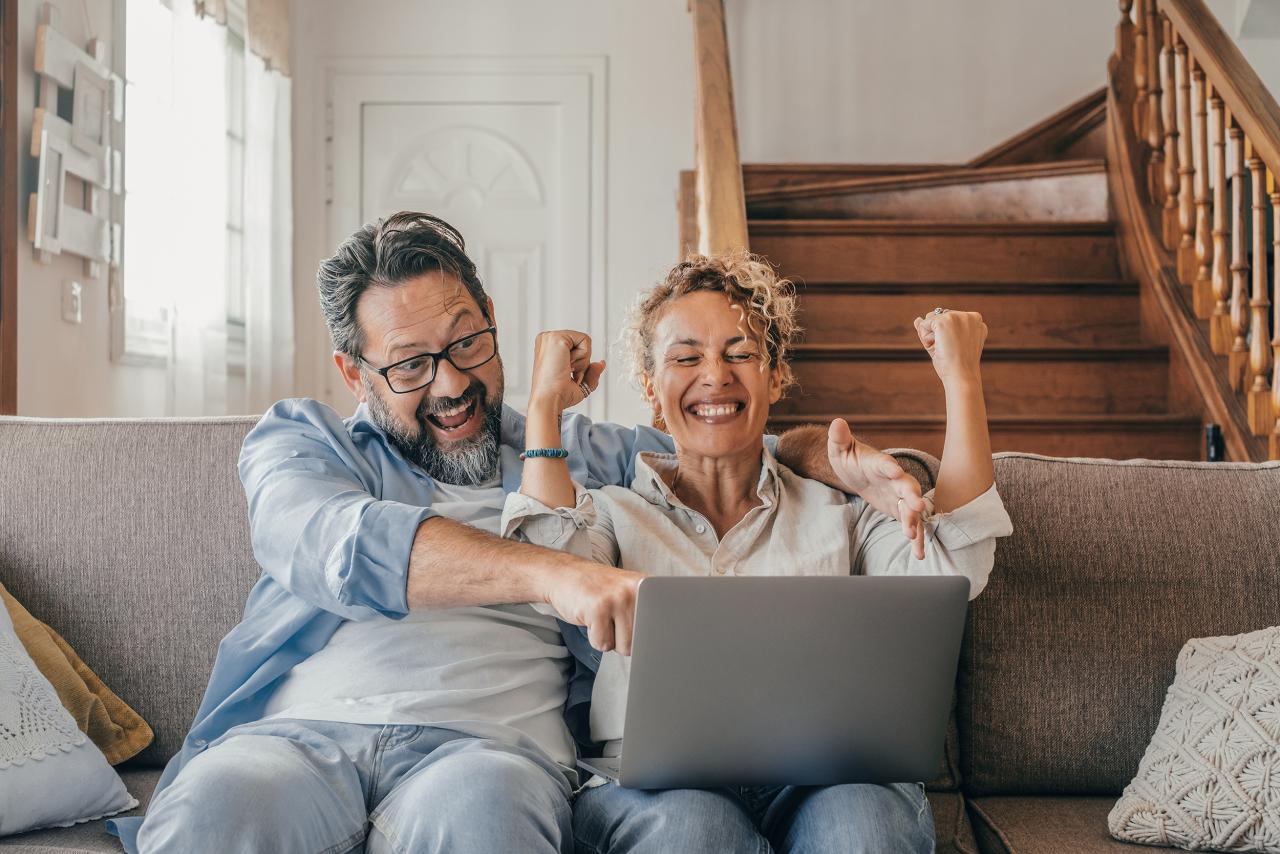 Ehepaar sitzt auf Sofa mit einem Laptop und freut sich