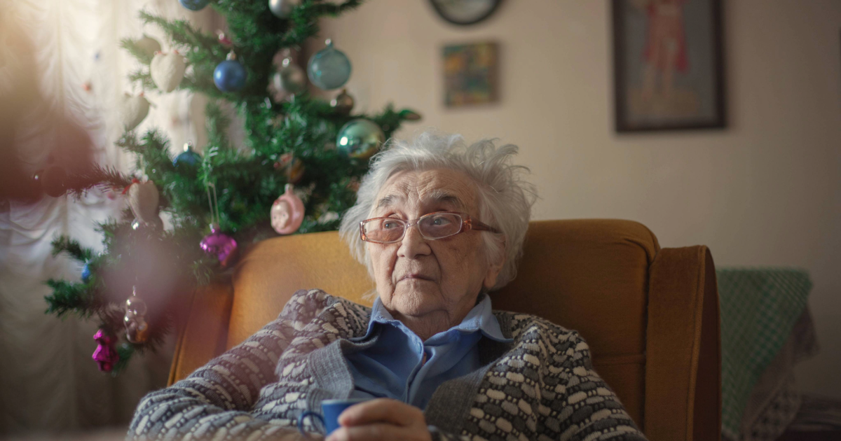 Ältere Frau sitzt auf Sessel, Weihnachtsdekoration im Hintergrund