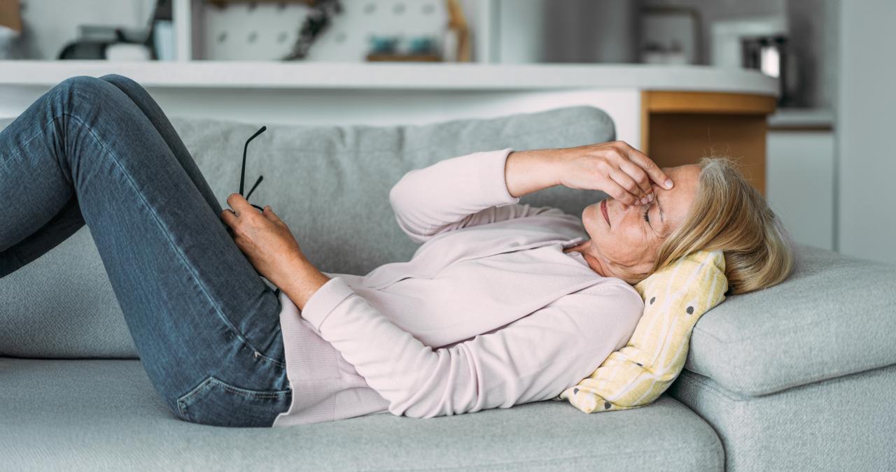 Frau liegt erschöpft auf dem Sofa und hält die Hand vor die Augen