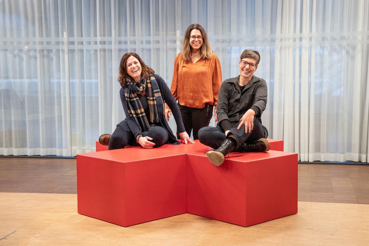 Drei Mitarbeiterinnen sitzen auf dem Roten Sitzkreuz.