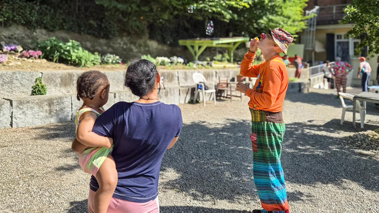 Eine geflüchtete Frau und ihre Tochter beobachten einen Clown.