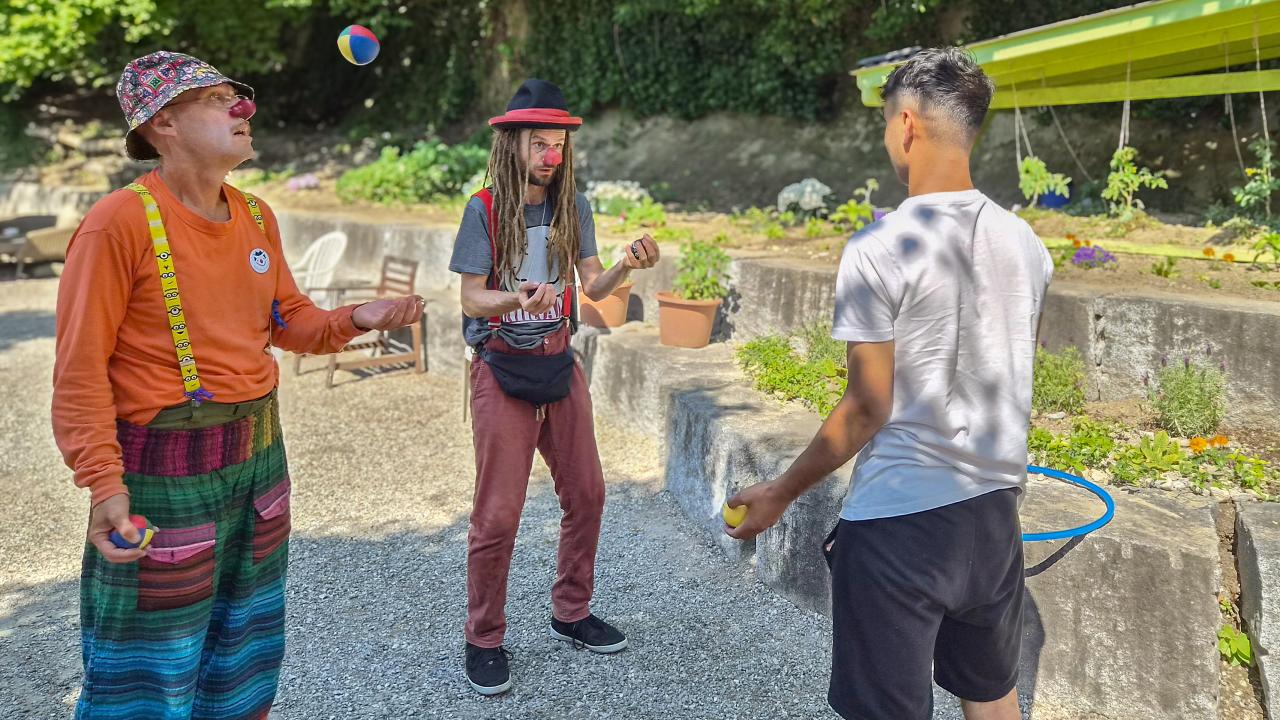 Clowns werfen einem jungen Geflüchteten Jonglierbälle zu.