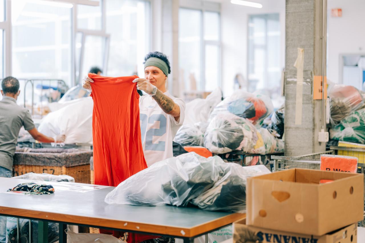 Mann schaut sich im Sortierbetrieb bei la trouvaille ein gespendetes oranges Kleid an.