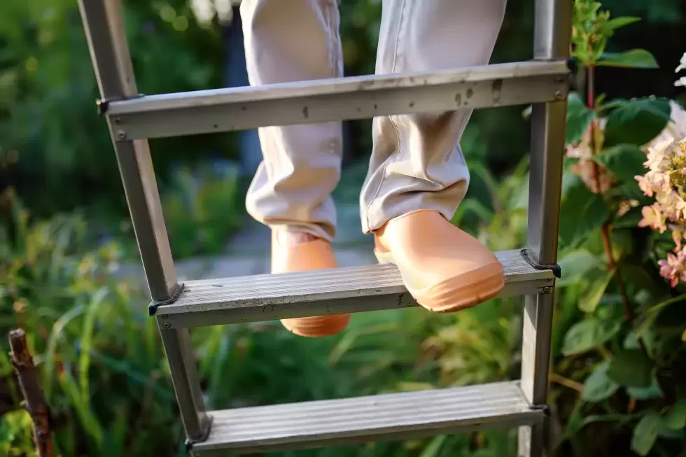 Personne âgée grimpant une échelle de jardin avec des chaussures en caoutchouc.