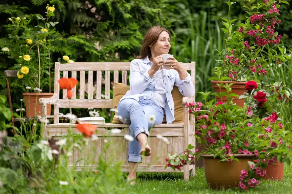 Eine Frau auf einer Gartenbank mit einer Teetasse. Sie macht einen eher müden Eindruck.