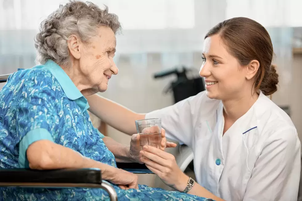 Pflegehelfende reicht einer alten Dame ein Glas Wasser