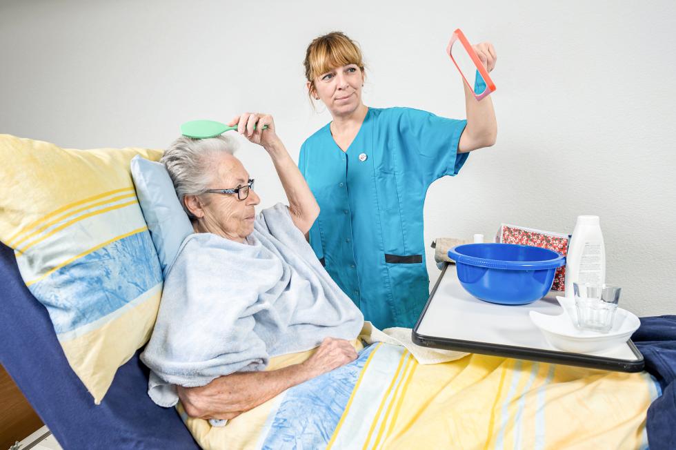 Eine Pflegehelfende unterstützt eine bettlägerige Frau bei der Morgenpflege.