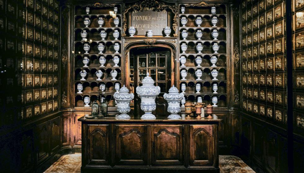 Ancienne pharmacie avec des armoires en bois jusqu'au plafond et des récipients de porcelaine.