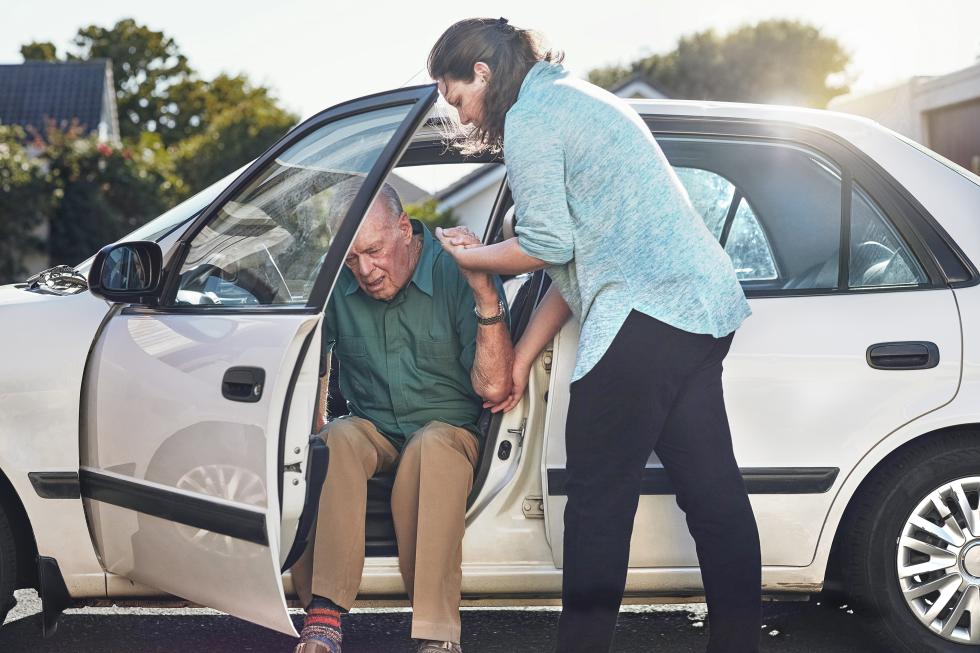 Eine Frau hilft einen älteren Mann beim Aussteigen aus dem Auto.