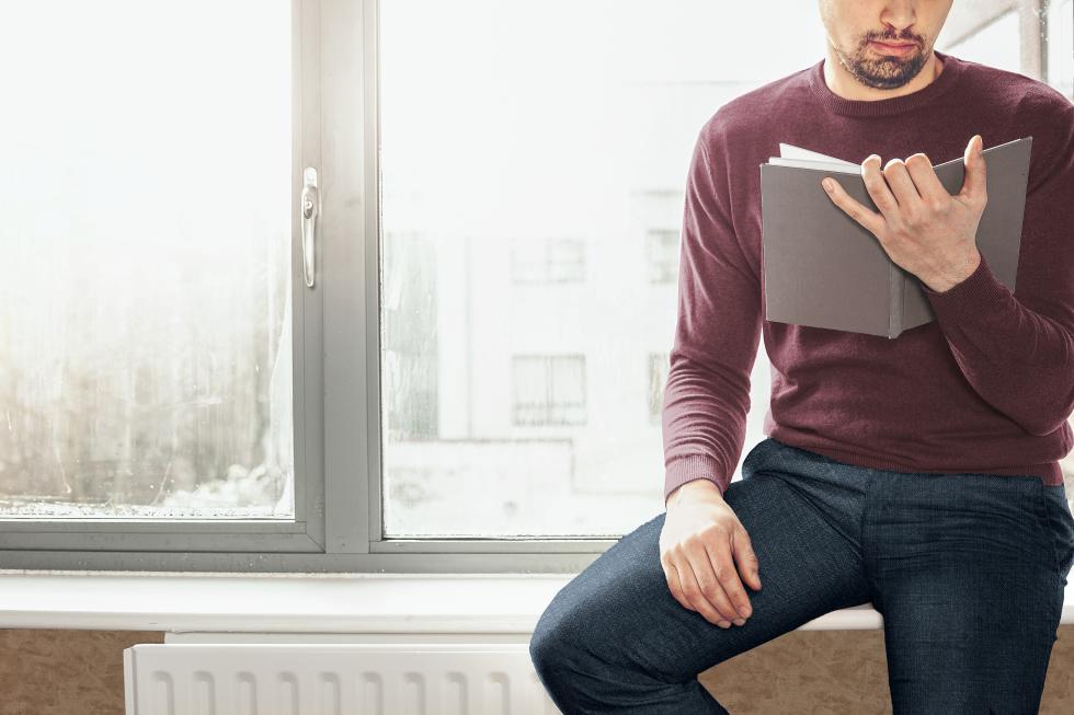 Mann sitzt vor einem Fenster und liest ein Buch