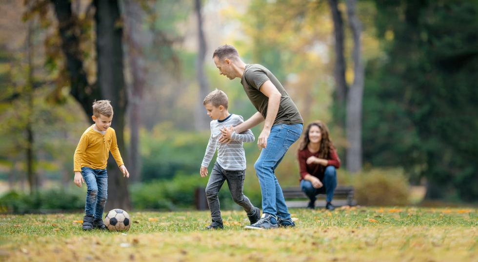 Ein Vater spielt im Park mit zwei Kindern Fussball