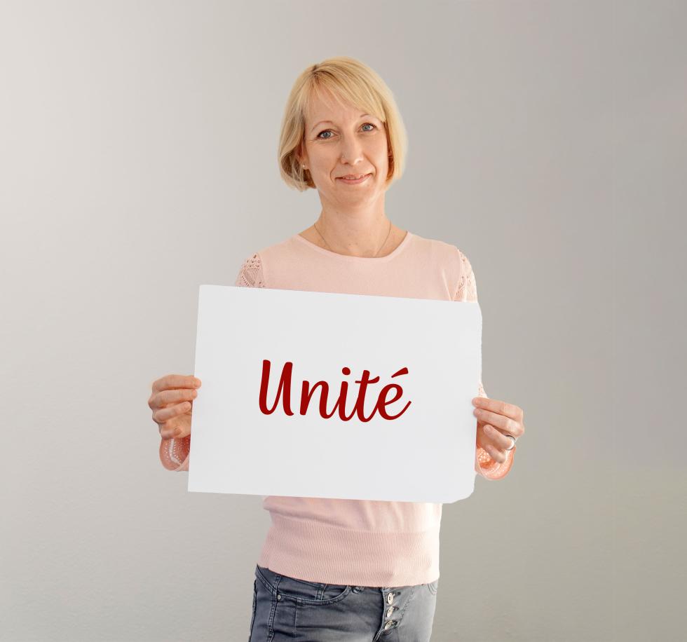 Cornelia Bischoff, ergothérapeute à la Croix-Rouge suisse (CRS), tient face à la caméra une affiche sur laquelle il est écrit Unité.