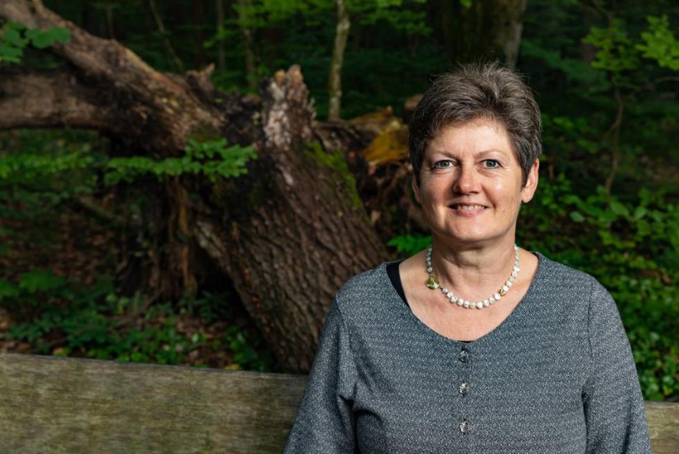 Renate Lorenz steht vor einem Waldhintergrund und schaut in die Kamera